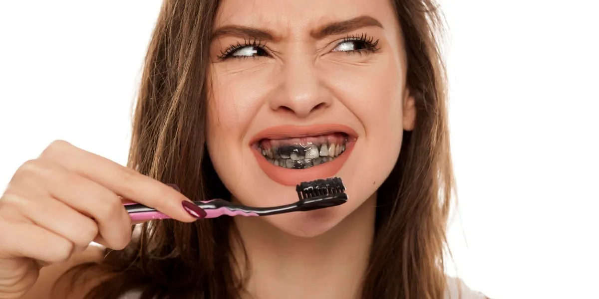 young woman brushing her teeth with a black tooth paste with active charcoal, and black tooth brush on white background young woman brushing her teeth with a black tooth paste with active charcoal, and black tooth brush on white background