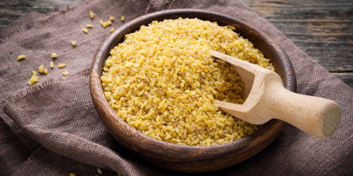 raw bulgur in wooden bowl on brown textile, close up shot healthy, dietary, vegan, gluten free product