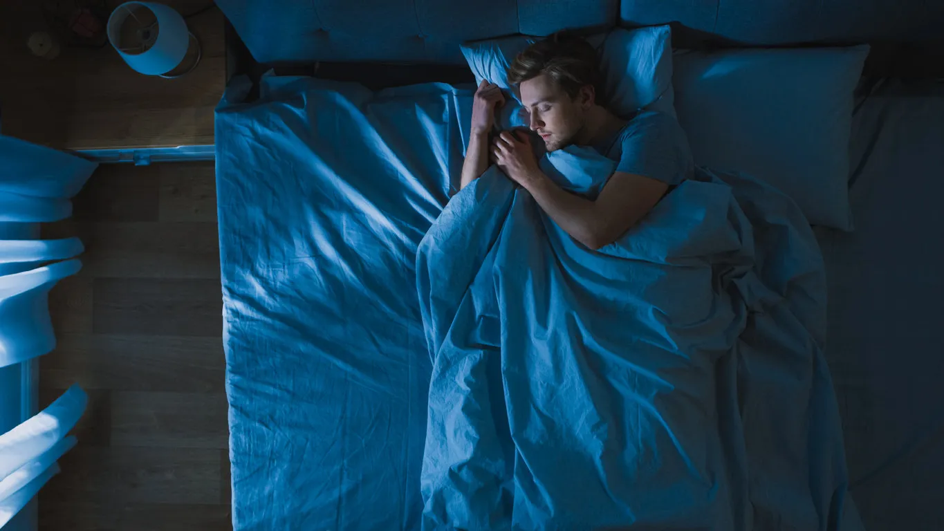 top view of handsome young man sleeping cozily on a bed in his bedroom at night blue nightly colors with cold weak lamppost light shining through the window top view of handsome young man sleeping cozily on a bed in his bedroom at night blue nightly colors with cold weak lamppost light shining through the window