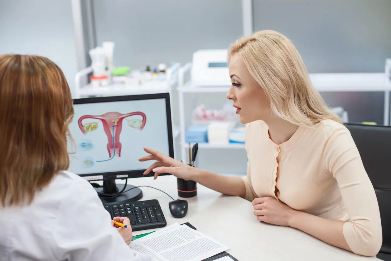 cheerful young woman is asking advice in her gynecologist she is sitting at the desk and pointing finger at the computer with uterus picture lady is listening to doctor with concentration cheerful young woman is asking advice in her gynecologist she is sitting at the desk and pointing finger at the computer with uterus picture lady is listening to doctor with concentration