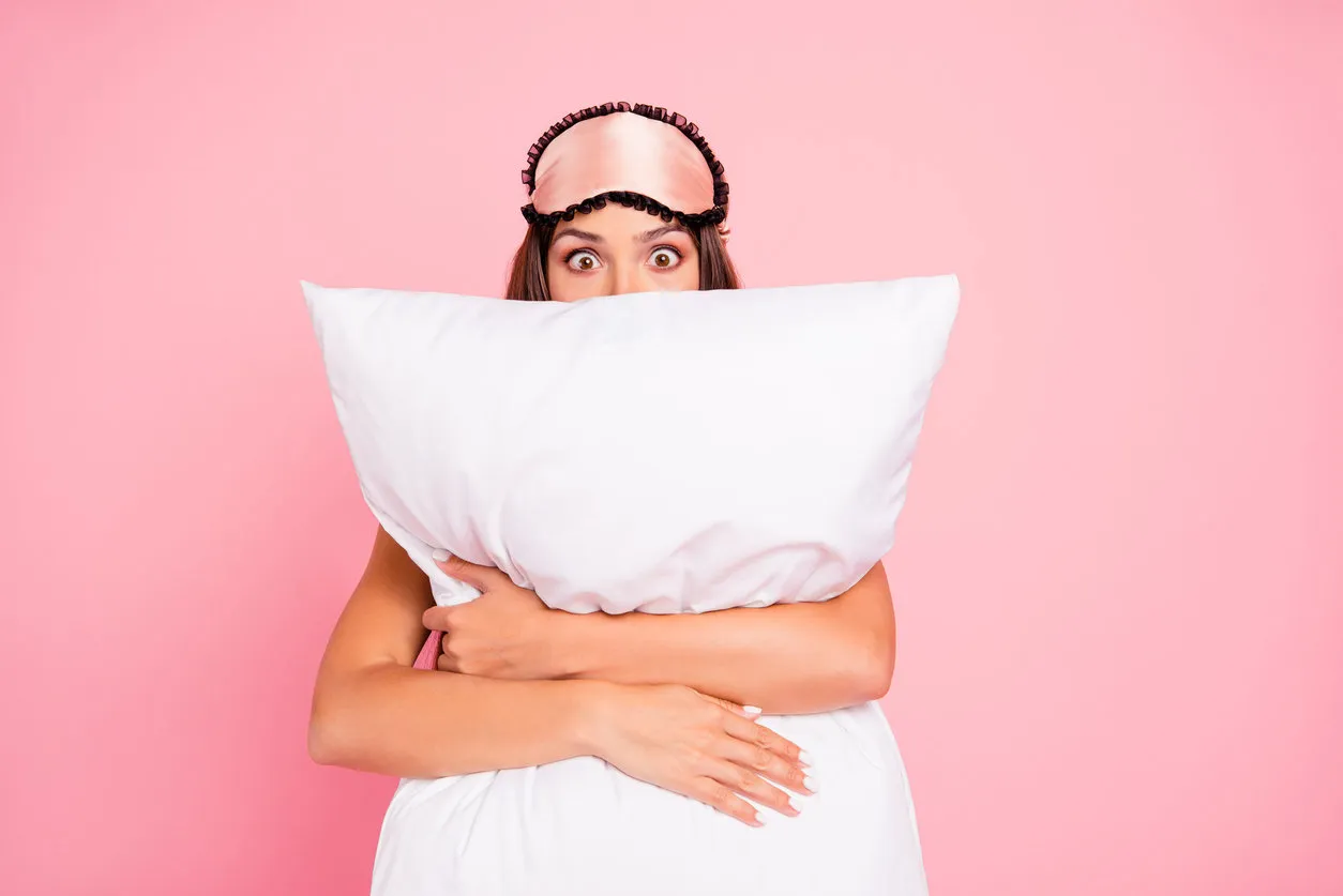 young gorgeous shocked lady wearing eye mask, hugging pillow, hiding isolated over pink pastel background young gorgeous shocked lady wearing eye mask, hugging pillow, hiding isolated over pink pastel background