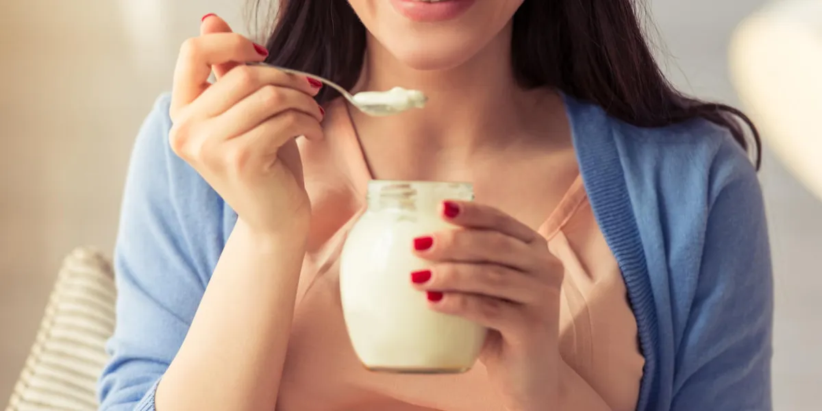 image recadrée de belle femme enceinte, manger du yogourt et souriant tout en étant assis à la maison image recadrée de belle femme enceinte, manger du yogourt et souriant tout en étant assis à la maison
