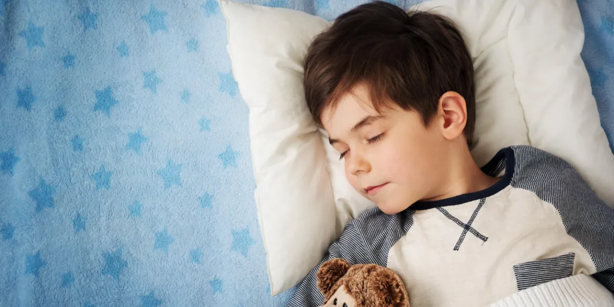 enfant de six ans, dormir dans son lit sur l'oreiller avec réveil et un ours en peluche enfant de six ans, dormir dans son lit sur l'oreiller avec réveil et un ours en peluche