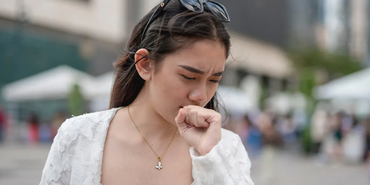 a young asian woman coughs while walking around the city urban air pollution issues or allergens a young asian woman coughs while walking around the city urban air pollution issues or allergens