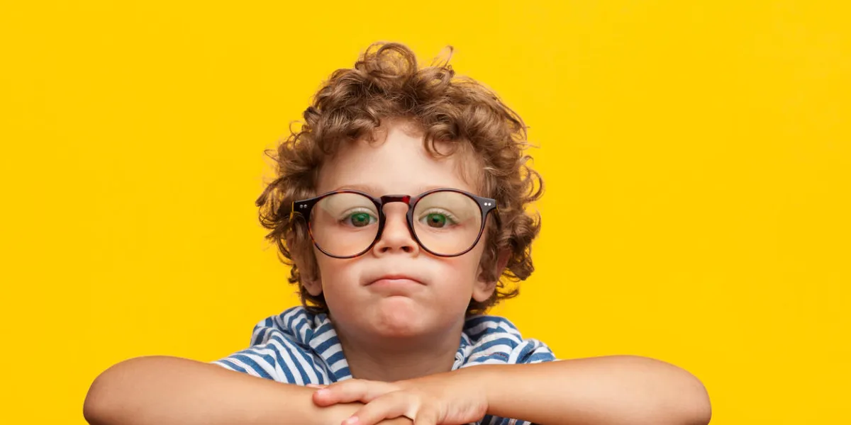 little curly boy in glasses leaning on wooden box looking at camera on orange background little curly boy in glasses leaning on wooden box looking at camera on orange background